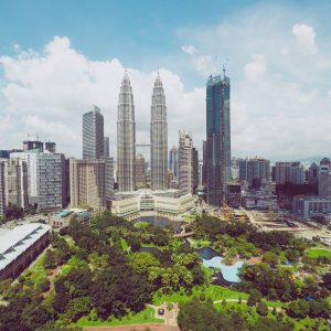 An aerial shot of Petronas Twin Towers near skyscrapers and trees under a blue sky in Kuala Lumpur, Malaysia